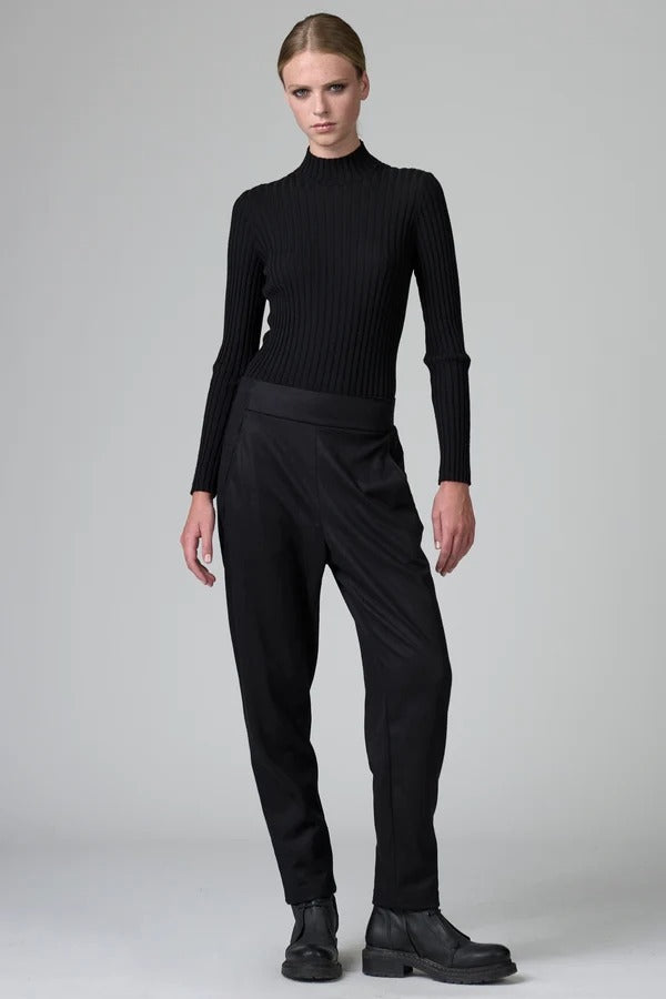 Front view of black slim fit trousers on model wearing black top and boots, against a grey background.