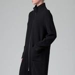 Side view of black/anthracite straight coat on model wearing black pants, against a grey background.