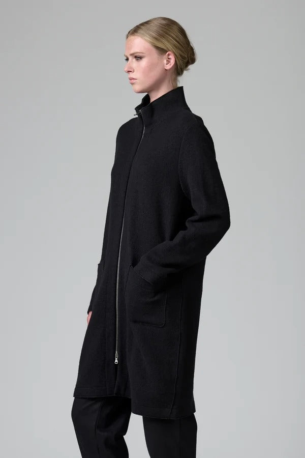 Side view of black/anthracite straight coat on model wearing black pants, against a grey background.