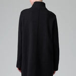 Back view of black/anthracite straight coat on model wearing black pants, against a grey background.