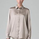 Front view of stone silk satin regular fit shirt on model wearing chalk pants, against a grey background.