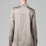Back view of stone stretch silk satin regular fit shirt on model wearing chalk pants against a grey background 