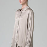 Side view of stone stretch silk satin regular fit shirt on model wearing chalk pants, against a grey background.