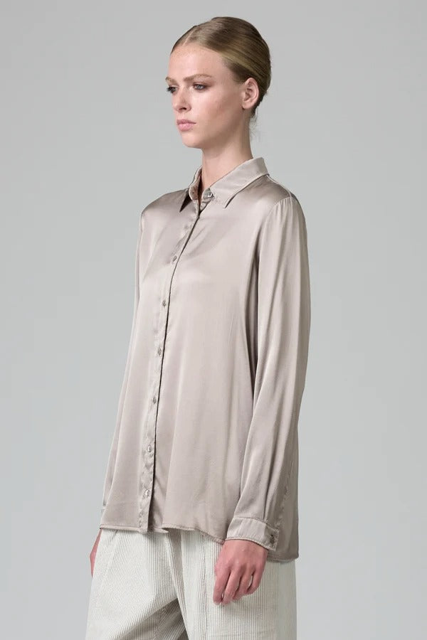 Side view of stone stretch silk satin regular fit shirt on model wearing chalk pants, against a grey background.
