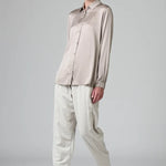Front view of stone stretch silk satin regular fit shirt on model wearing chalk pants, against a grey background.