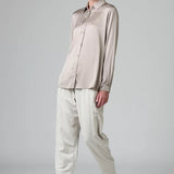 Front view of stone stretch silk satin regular fit shirt on model wearing chalk pants, against a grey background.