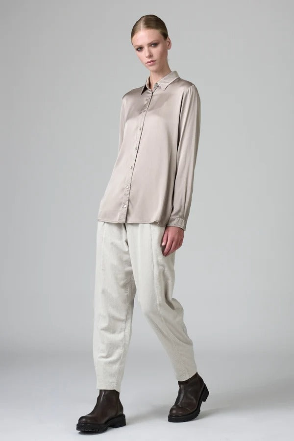 Front view of stone stretch silk satin regular fit shirt on model wearing chalk pants, against a grey background.