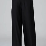 Front view of black stretch wide leg trousers on model wearing black top and boots, against a grey background.