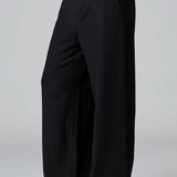 Side view of black stretch wide leg trousers on model wearing black top and boots, against a grey background.