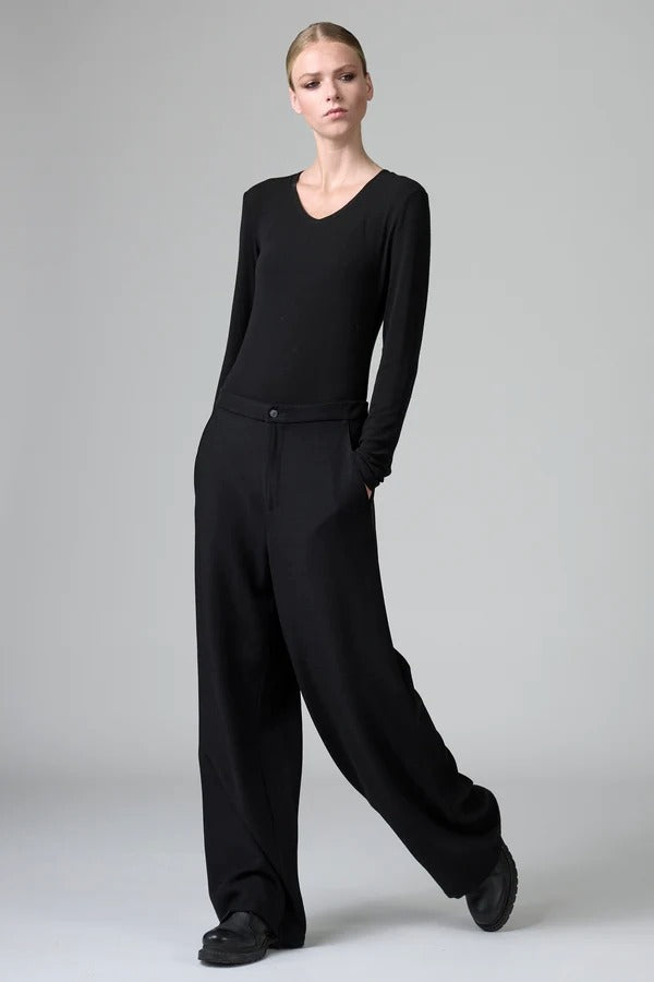 Front view of black stretch wide leg pants on model wearing black top and boots, against a grey background.