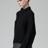 Side view of black wool chain stitch knit ribbed turtleneck on model wearing grey pants, against a grey background.