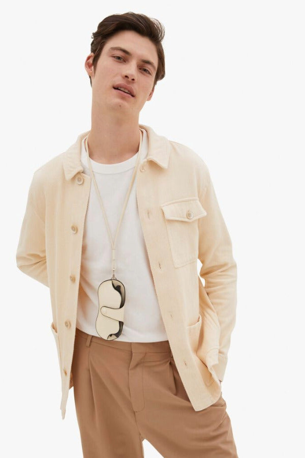 Back view of white valextra glasses case with lanyard on model wearing white t-shirt with orange trousers, against a white background.