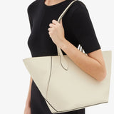 Front view of white valextra's small vivi shopping bag on model wearing black shirt and pants, against a white background.