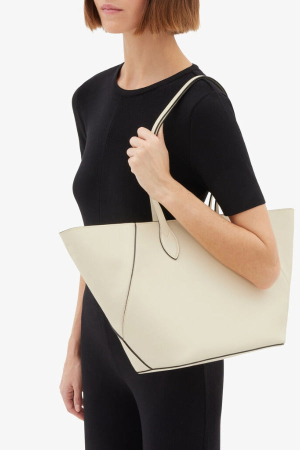 Front view of white valextra's small vivi shopping bag on model wearing black shirt and pants, against a white background.
