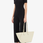 Front alternate view of white valextra's small vivi shopping bag on model wearing black shirt and pants, against a white background.