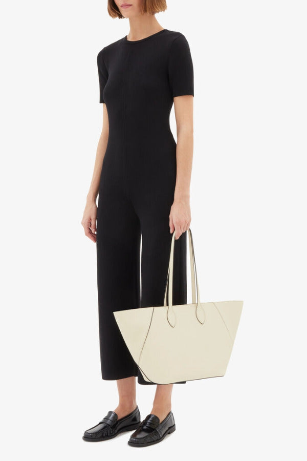 Front alternate view of white valextra's small vivi shopping bag on model wearing black shirt and pants, against a white background.