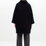 Back view of black bonnet drivers down coat on model wearing grey pants, against a white background.