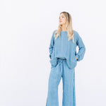 Front view of denim pants with velvet ribbon on model wearing denim tunic and black sandals, against a white background.