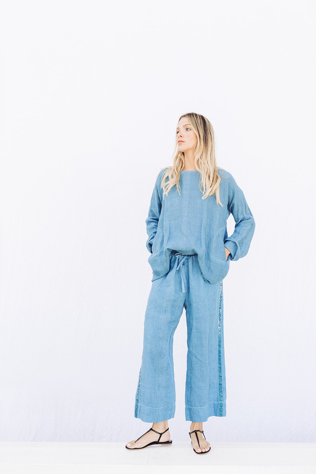 Front view of denim pants with velvet ribbon on model wearing denim tunic and black sandals, against a white background.