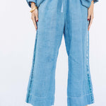 Front closeup view of denim pants with velvet ribbon on model wearing denim tunic and black sandals, against a white background.