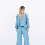 Back view of denim pants with velvet ribbon on model wearing denim tunic and black sandals, against a white background.